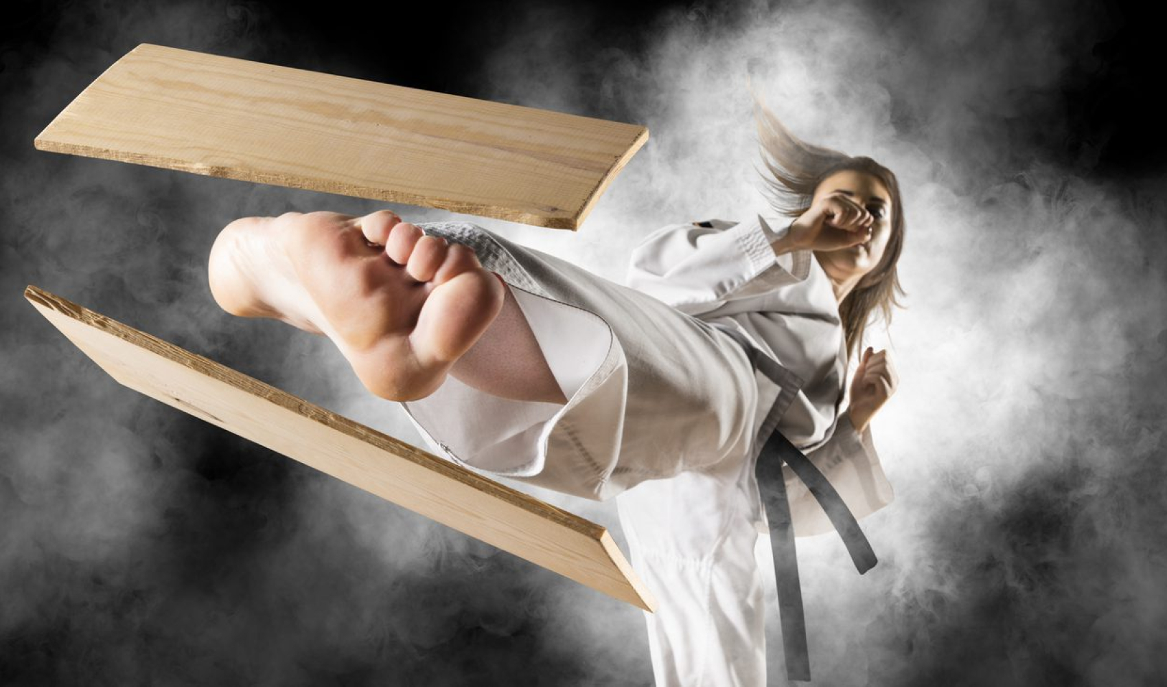 Woman in kimono practicing. Fighter concept. Breaking board. Smoke background